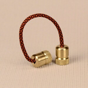 May include: Two brass fidget toys with a black and orange cord connecting them. The toys are cylindrical with a textured surface.