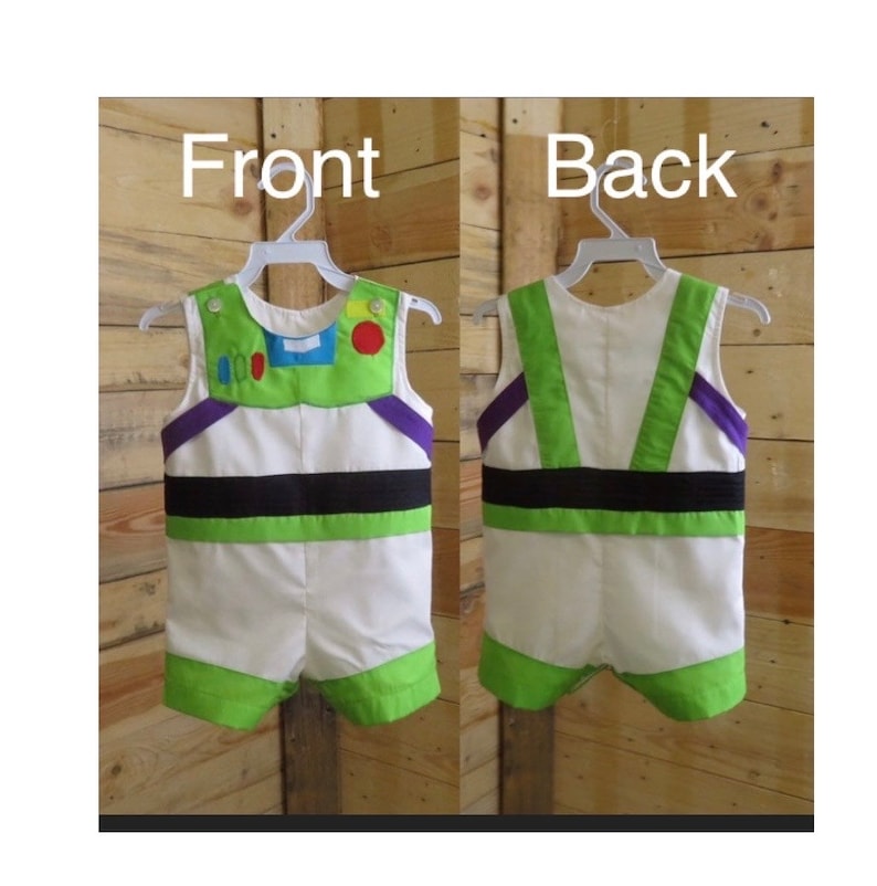 Puede incluir: Un pelele blanco y verde con el tema de Buzz Lightyear, mostrado por delante y por detr&aacute;s. La parte delantera presenta una pieza verde en el pecho con detalles coloridos, acentos morados y una banda negra. La parte trasera tiene acentos verdes y morados. El pelele est&aacute; en una percha blanca.