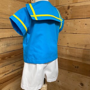 May include: A blue and white sailor-style outfit for a child. The shirt has a blue collar with yellow trim and short sleeves. The shorts are white.