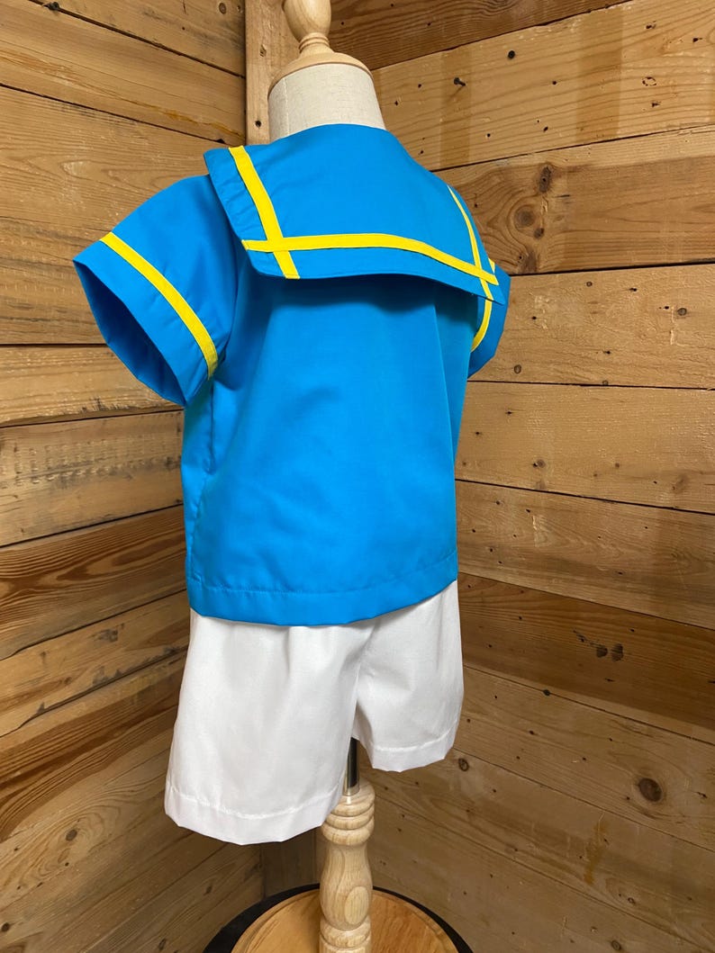 May include: A blue and white sailor-style outfit for a child. The shirt has a blue collar with yellow trim and short sleeves. The shorts are white.