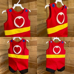 Puede incluir: Romper rojo y amarillo con dise&ntilde;o de coraz&oacute;n blanco. Botones azules en los hombros y una franja amarilla en el pecho. La parte inferior del romper es negra.