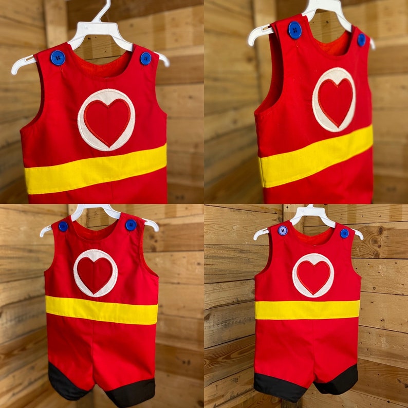 Puede incluir: Romper rojo y amarillo con dise&ntilde;o de coraz&oacute;n blanco. Botones azules en los hombros y una franja amarilla en el pecho. La parte inferior del romper es negra.