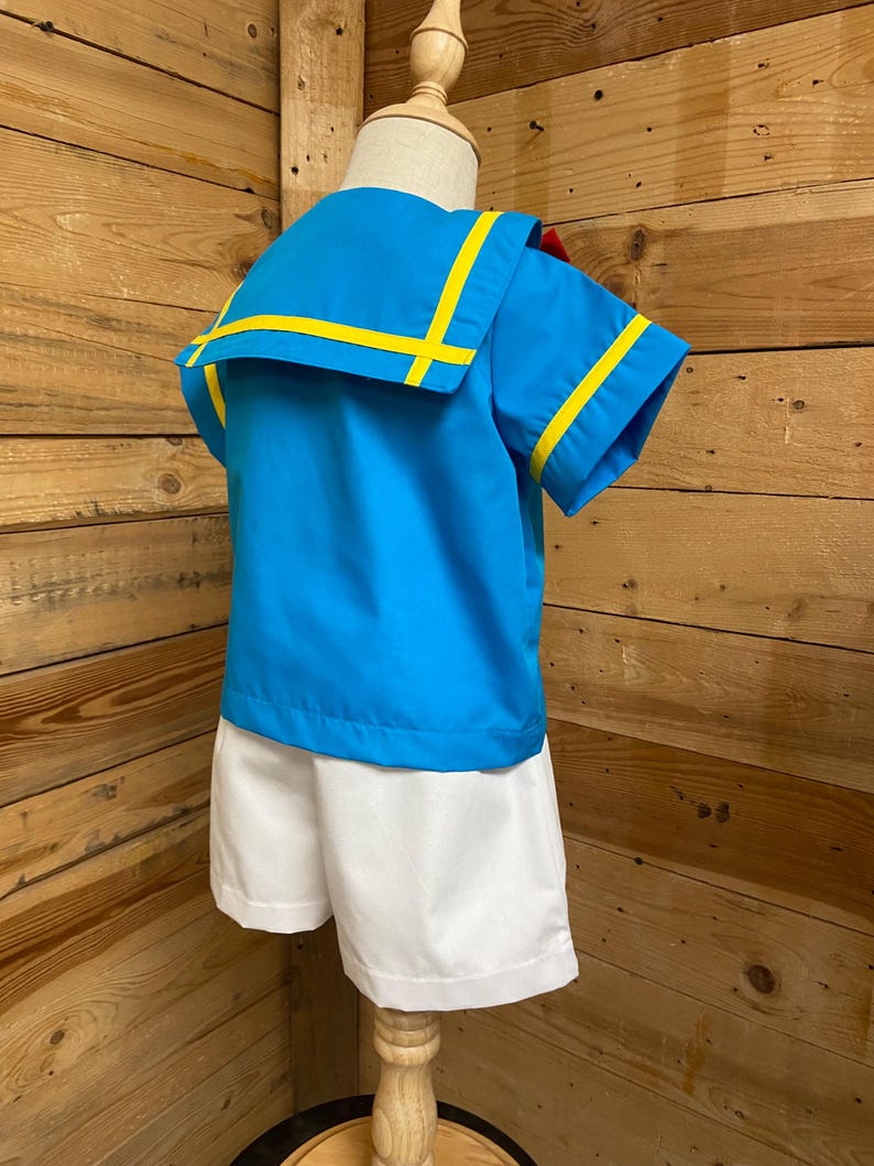 May include: A blue and white sailor outfit for a child. The shirt has yellow trim and a white collar. The shorts are white.