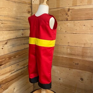 Peut inclure: Un costume de pompier rouge et jaune pour enfants. Le costume comprend un haut et un pantalon rouges, avec une bande jaune sur la poitrine et une bordure noire aux chevilles. Le costume est pr&eacute;sent&eacute; sur un mannequin.