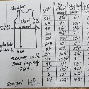 May include: Handwritten size chart for a dress, with measurements in inches. The chart includes sizes from 3M to 6T, detailing chest, waist, shoulder, and total dress length. The text "Cowgirl Pink" is written at the bottom.
