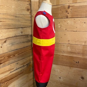 Peut inclure: Un costume rouge avec une bande jaune et un motif de cercle blanc. Le costume a un bouton bleu sur l'&eacute;paule et un ourlet noir. Le costume est pr&eacute;sent&eacute; sur un mannequin.