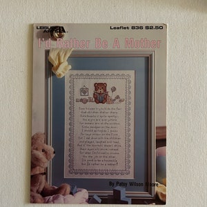 May include: A cross-stitch pattern titled "I'd Rather Be A Mother" featuring a teddy bear reading a book. The pattern is framed and includes a poem. The cover also shows a small teddy bear and a pair of yellow gloves.
