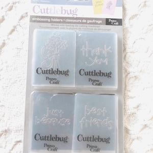 May include: A set of four translucent Cuttlebug embossing folders by Provo Craft in original packaging. The folders feature designs of a flower bouquet, the text thank you, the text just because, and the text best friends, all in a clear plastic.