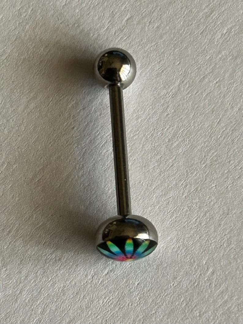 May include: A silver-toned barbell body jewelry piece featuring a smooth spherical top bead and a flat circular bottom end. The bottom end displays a vibrant, multi-colored radial flower pattern with shades of blue, green, yellow, and pink.