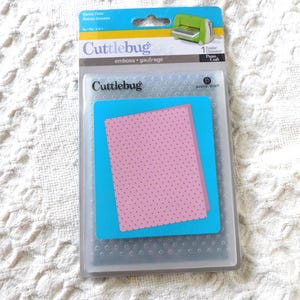 May include: A Cuttlebug Swiss Dots embossing folder in its original retail packaging. The clear plastic folder features a repeating dot pattern. The packaging includes blue and white branding with the text Cuttlebug, Swiss Dots, and Provo Craft.