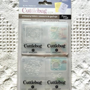 May include: A package of Cuttlebug embossing folders featuring flower designs. The package includes four folders with various floral patterns, including daisies and other flower arrangements. The packaging is clear plastic with the Cuttlebug and Provo Craft logos.