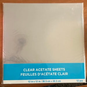 May include: A package of 12 clear acetate sheets, measuring 12 inches by 12 inches, or 30.5 centimeters by 30.5 centimeters. The package is labeled "CLEAR ACETATE SHEETS" and "FEUILLES D'ACÉTATE CLAIR".