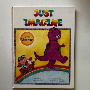 May include: A children's book cover featuring Barney the Dinosaur in purple, walking on a rainbow with a girl and her dog in a red wagon. The book title is "Just Imagine with Barney".