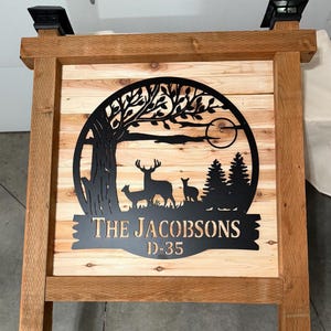 May include: A wooden sign with a black metal design featuring a tree, deer, and the text "The Jacobsons D-35".