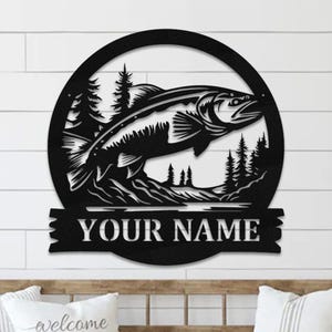 May include: Black metal wall art featuring a fish jumping out of the water with a forest scene in the background. The art includes a personalized nameplate that reads "YOUR NAME".