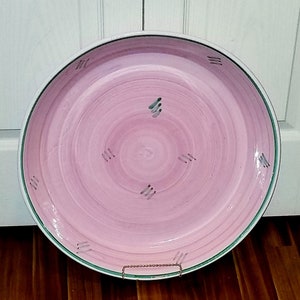 May include: A large, pink ceramic serving platter with a green rim and a swirl design. The platter has a white centre with a subtle green and grey pattern.