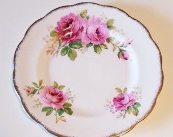 May include: A white porcelain plate with a gold rim and a floral design featuring pink roses.