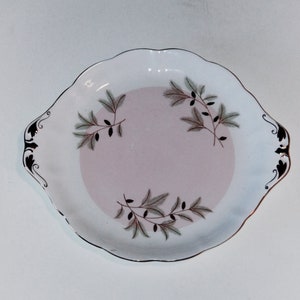 Puede incluir: Un plato de servir de cerámica blanca con un centro rosa y un borde dorado. El plato tiene un delicado diseño floral en tonos verdes y marrones.