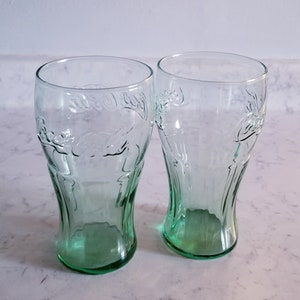 Puede incluir: Dos vasos de vidrio verde Coca-Cola con el logotipo de Coca-Cola en relieve en el lateral.