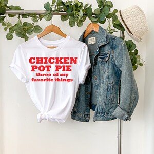 May include: White t-shirt with red text that reads "Chicken Pot Pie three of my favorite things".