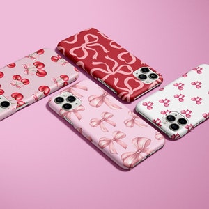 Peut inclure: Quatre étuis de téléphone différents avec des motifs variés. Les étuis présentent des nœuds roses et rouges, des cerises et un fond blanc. Les étuis sont tous pour l'iPhone 12 Pro Max.