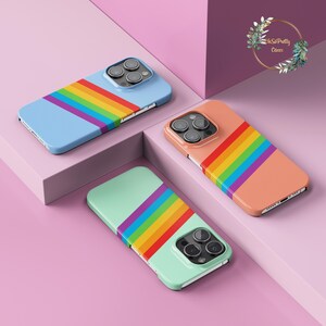 May include: Three smartphone cases featuring a diagonal rainbow stripe pattern. One case has a light blue base, one has a peach base, and one has a mint green base. Each case includes a cutout for a triple-lens camera system on the back.