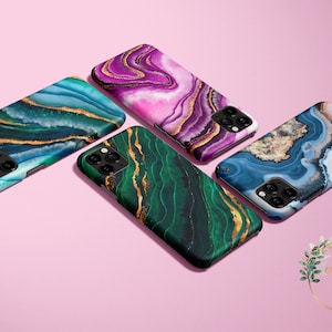 May include: Four different phone cases with a marble pattern. The cases are in shades of blue, green, pink, and purple with gold accents.