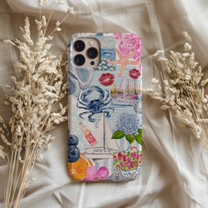 May include: A colorful phone case with a collage of images including a blue crab, a sailboat, a starfish, and a bottle of pink soda. The case has a white background with blue and pink stripes.