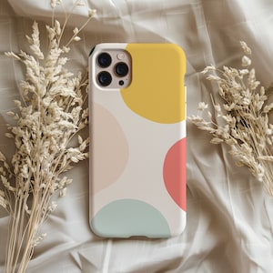 Può includere: Una custodia per telefono bianca con un motivo geometrico di cerchi in giallo, rosa, blu e verde. La custodia ha un ritaglio per l'obiettivo della fotocamera e un bordo nero.