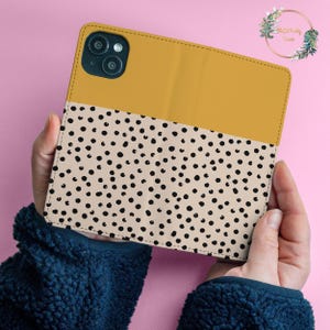 May include: A mustard yellow and beige phone case with a black polka dot pattern. The case has a cutout for the camera lens.