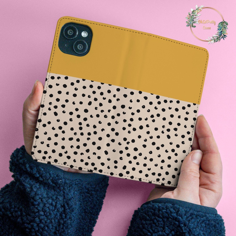 May include: A mustard yellow and beige phone case with a black polka dot pattern. The case has a cutout for the camera lens.