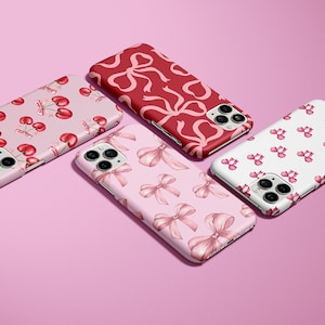 May include: Four different phone cases with various designs. The cases feature pink and red bows, cherries, and a white background. The cases are all for the iPhone 12 Pro Max.