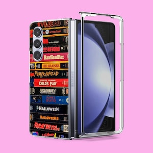 Puede incluir: Una funda transparente para teléfono con un diseño de cintas VHS de películas de terror. La funda tiene un borde negro y el texto "SAMSUNG" está impreso en el lateral. Las cintas incluyen títulos como "Evil Dead", "Pumpkinhead", "Child's Play" y "Halloween".