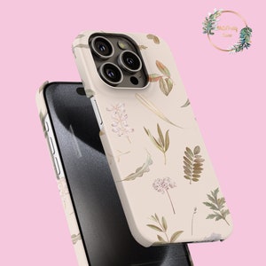 以下が含まれることがあります： 緑、茶色、白の色の葉と花が描かれた花柄のベージュの携帯電話ケース。ケースはトリプルカメラシステムを搭載した携帯電話用に設計されています。