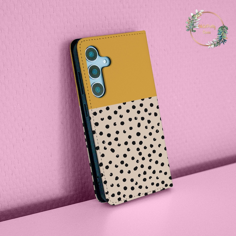 May include: A mustard yellow and white phone case with a black polka dot pattern. The case has a flap that covers the screen of the phone.