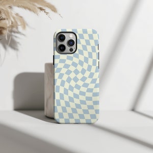 Puede incluir: Una funda para teléfono a cuadros azules y crema con un patrón de remolino. La funda está diseñada para un teléfono con una protuberancia de cámara.