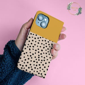 May include: A mustard yellow and beige phone case with a black polka dot pattern. The case has a cutout for the camera lens.