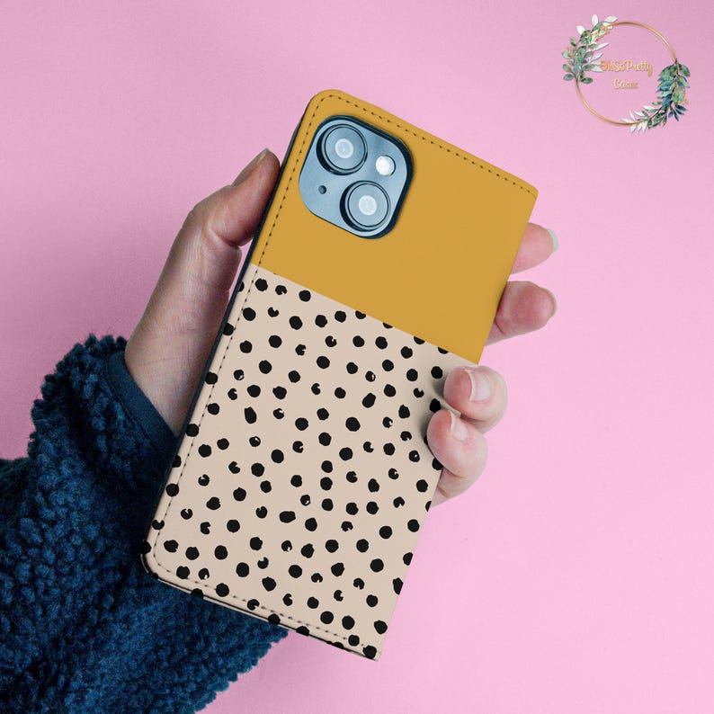 May include: A mustard yellow and beige phone case with a black polka dot pattern. The case has a cutout for the camera lens.