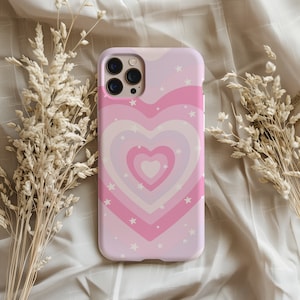 May include: A pink and white phone case with a heart design and white stars. The heart is made up of concentric circles of pink and white.