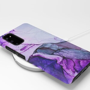 May include: A purple and blue abstract phone case with a white wireless charging pad and a white charging cable.