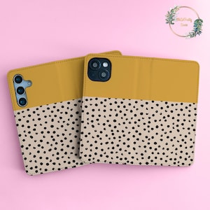 May include: Two mustard yellow phone cases with a black and white polka dot pattern. The cases are made of leather and have a flap that covers the screen.