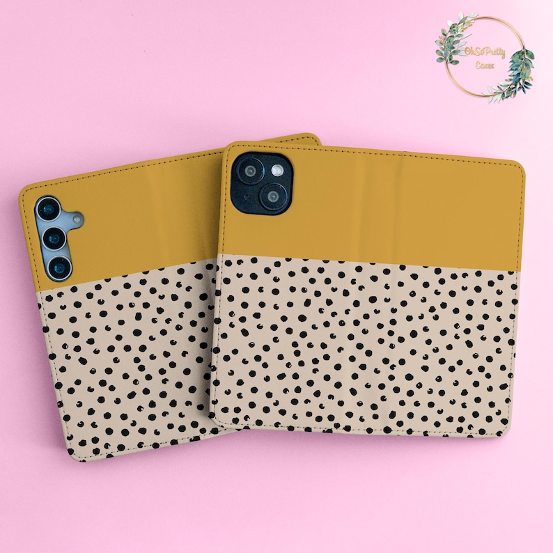 May include: Two mustard yellow phone cases with a black and white polka dot pattern. The cases are made of leather and have a flap that covers the screen.