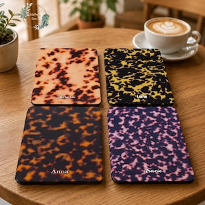 Puede incluir: Cuatro fundas rectangulares para lector electrónico con distintos patrones de carey en tonos ámbar, negro y amarillo, marrón oscuro, y morado y negro. Cada funda está personalizada con un nombre en letra cursiva blanca: Aurora, Lorie, Anna y Tracie.