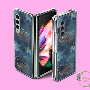 Puede incluir: Una funda transparente para teléfono con un diseño de galaxia y luna creciente en tonos azules y dorados. La funda está diseñada para un Samsung Galaxy Z Fold 3.