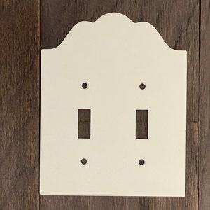 May include: White ceramic double light switch cover with an arched top and rounded edges.