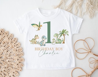 May include: White t-shirt with a green number one, green dinosaurs, and palm trees. The text "Birthday Boy Charlie" is printed on the shirt.