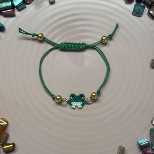 Puede incluir: Pulsera de cordón verde con un dije de rana de cuentas verdes y blancas y cuentas doradas.