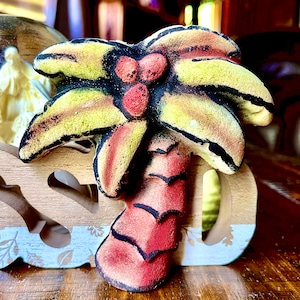 Könnte beinhalten: Dekorative Palmenfigur mit gelben, roten und schwarzen Akzenten. Die Palme ist auf einem Holzsockel mit den ausgeschnittenen Buchstaben "SO" montiert. Der Sockel hat ein Blumendesign und einen hellblauen Rand.