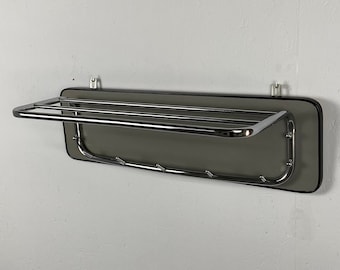 Può includere: Un appendiabiti cromato con uno scaffale e ganci montati su una parete bianca.