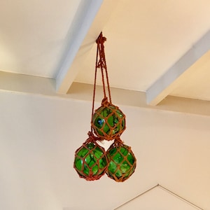 Op de afbeelding: Drie groene glazen drijvers met bruin netwerk hangend aan het plafond.